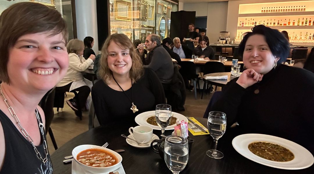 Three smiling women sitting at a restaurant table with plates of soup and glasses of water.